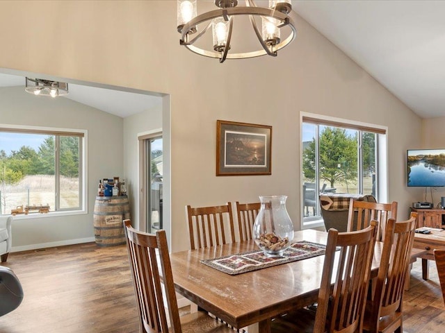 dining space with a chandelier, plenty of natural light, high vaulted ceiling, wood finished floors, and baseboards