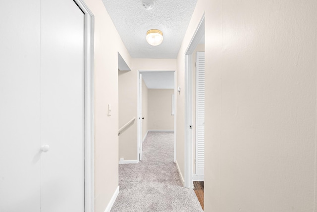 corridor with light carpet and a textured ceiling