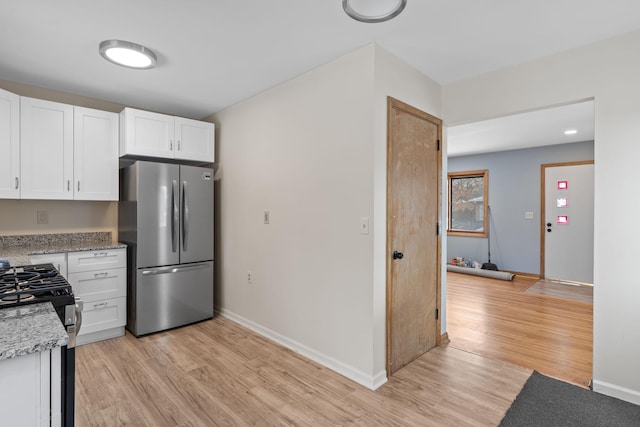 kitchen with white cabinets, light hardwood / wood-style flooring, gas stove, and stainless steel refrigerator