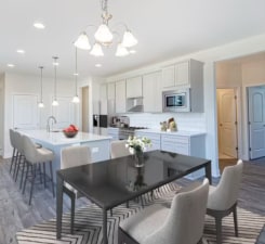 kitchen with stainless steel microwave, hanging light fixtures, dark wood-type flooring, a kitchen island with sink, and wall chimney range hood