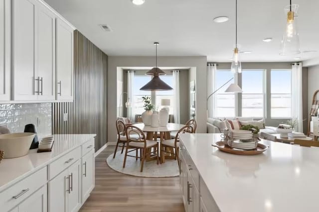 kitchen with white cabinetry, light hardwood / wood-style flooring, decorative backsplash, and pendant lighting