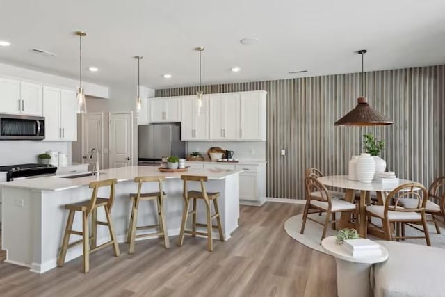 kitchen featuring sink, white cabinets, hanging light fixtures, a kitchen island with sink, and stainless steel appliances