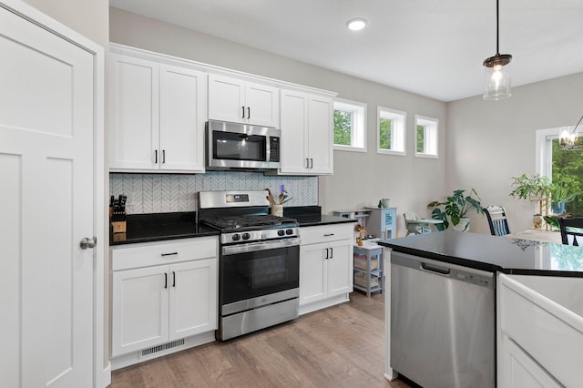 kitchen featuring appliances with stainless steel finishes, hanging light fixtures, decorative backsplash, and white cabinets