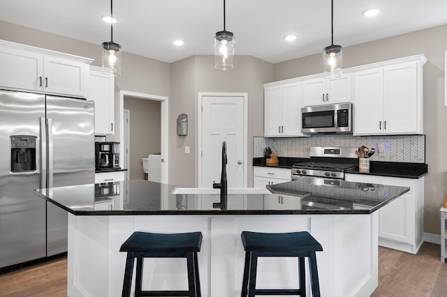 kitchen featuring a center island with sink, light wood-type flooring, pendant lighting, stainless steel appliances, and white cabinets