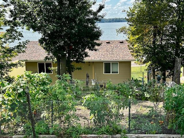 back of property with roof with shingles, a vegetable garden, and a water view