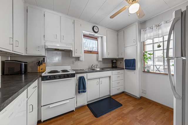 kitchen with dark countertops, a sink, under cabinet range hood, and white appliances