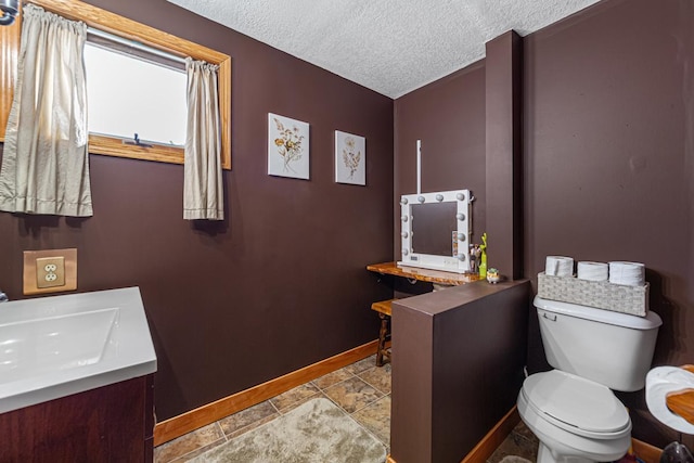 bathroom featuring stone finish floor, toilet, vanity, baseboards, and a textured ceiling