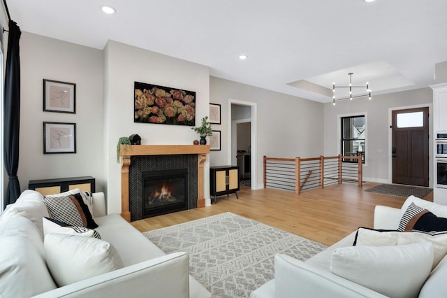 living room featuring a fireplace, light wood-type flooring, a tray ceiling, and an inviting chandelier