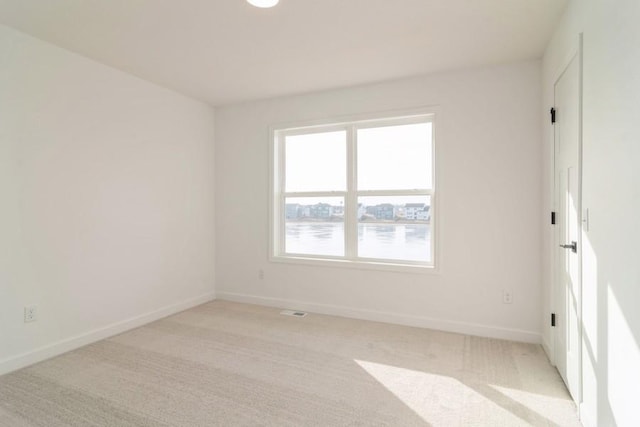 empty room featuring a water view and light colored carpet