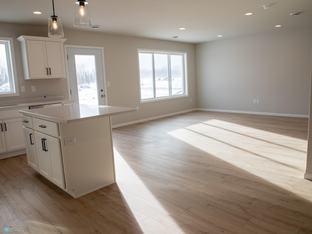 kitchen with white cabinetry, decorative light fixtures, a center island, and light wood-type flooring