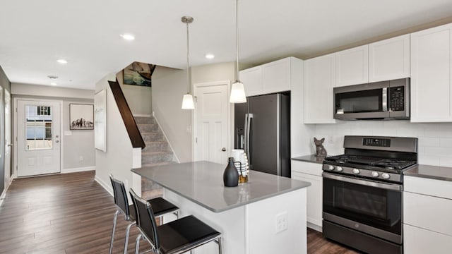 kitchen featuring appliances with stainless steel finishes, a kitchen island, decorative light fixtures, a kitchen bar, and white cabinetry