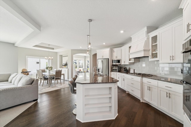 kitchen with an island with sink, stainless steel appliances, dark stone counters, pendant lighting, and white cabinets