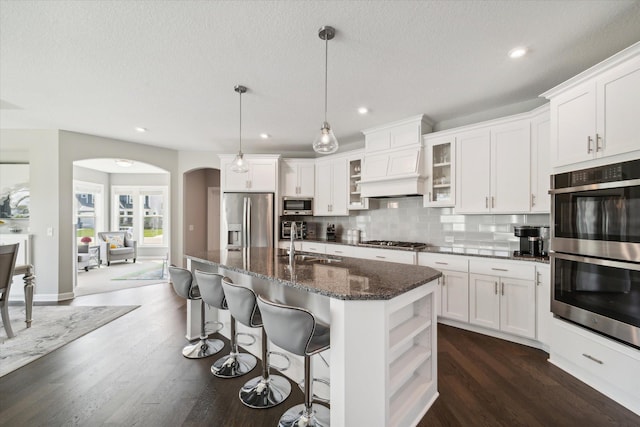 kitchen with stainless steel appliances, a kitchen island with sink, hanging light fixtures, white cabinets, and sink