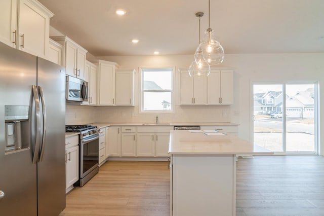 kitchen with decorative light fixtures, white cabinets, appliances with stainless steel finishes, and light hardwood / wood-style floors