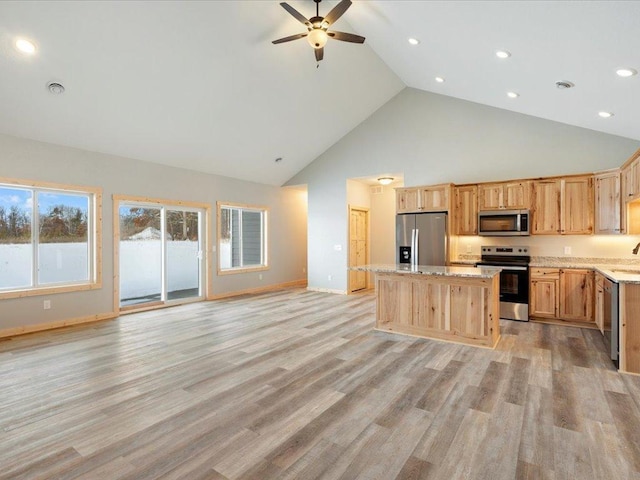 kitchen with light stone countertops, a kitchen island, stainless steel appliances, light wood-type flooring, and high vaulted ceiling