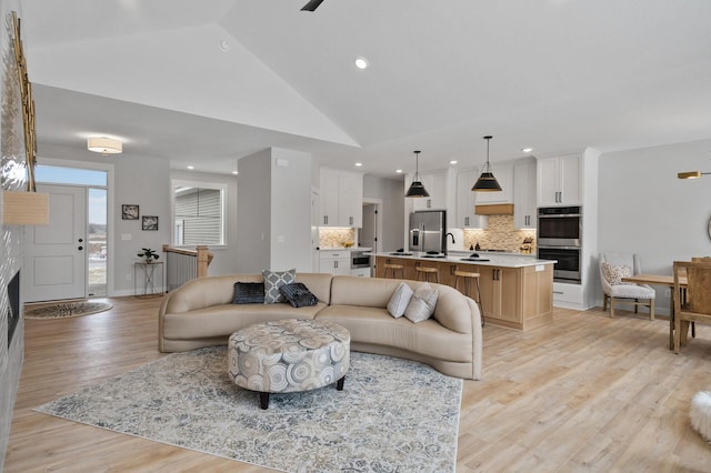 living room with light wood-type flooring, sink, and high vaulted ceiling