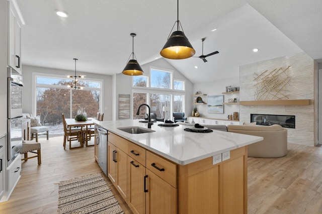 kitchen with a center island with sink, appliances with stainless steel finishes, a large fireplace, hanging light fixtures, and sink