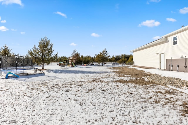 yard layered in snow featuring a playground and a trampoline