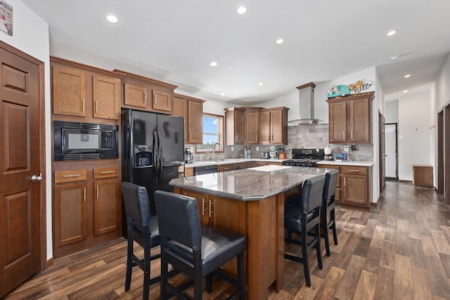 kitchen featuring sink, black appliances, a center island, a kitchen breakfast bar, and wall chimney range hood