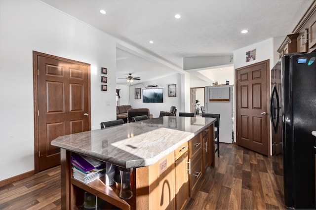 kitchen with light stone countertops, black fridge, a center island, and dark hardwood / wood-style floors