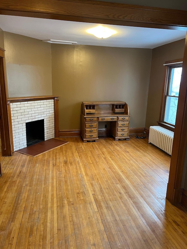 unfurnished living room with light hardwood / wood-style floors, radiator heating unit, and a brick fireplace