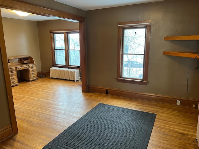 spare room featuring light hardwood / wood-style floors, radiator heating unit, and a healthy amount of sunlight