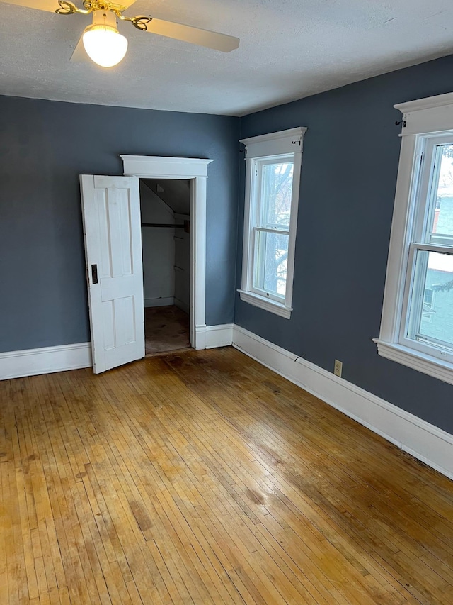 unfurnished bedroom featuring a walk in closet, ceiling fan, light hardwood / wood-style flooring, and a textured ceiling