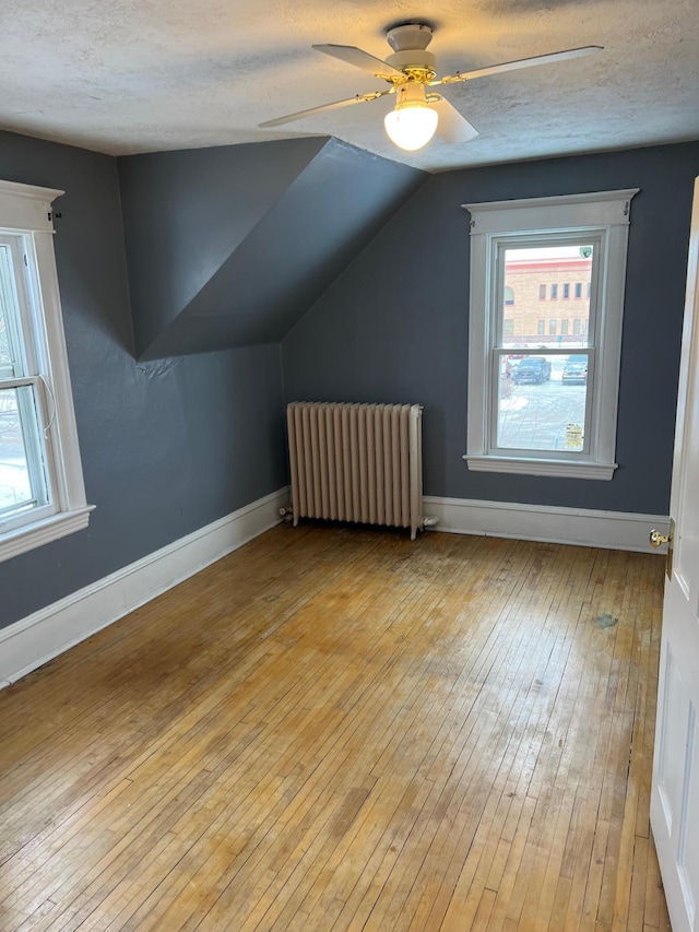 bonus room with vaulted ceiling, ceiling fan, light wood-type flooring, radiator, and a textured ceiling