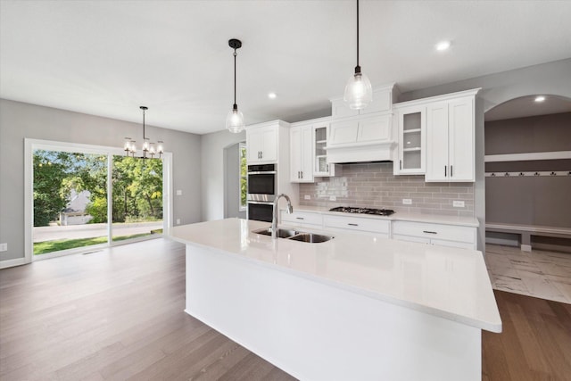 kitchen with tasteful backsplash, pendant lighting, sink, an island with sink, and white cabinets