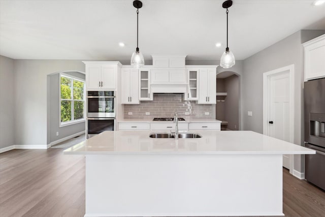 kitchen with white cabinets, decorative backsplash, sink, hanging light fixtures, and a center island with sink