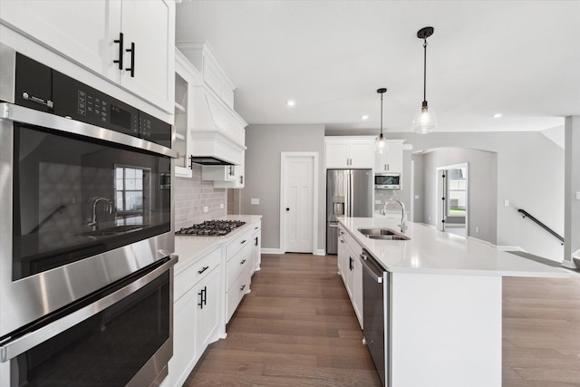 kitchen with decorative light fixtures, white cabinetry, an island with sink, sink, and backsplash