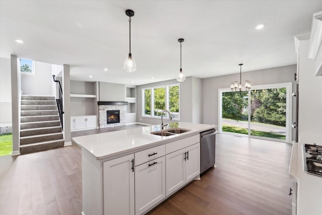 kitchen featuring white cabinets, an island with sink, sink, hanging light fixtures, and stainless steel dishwasher