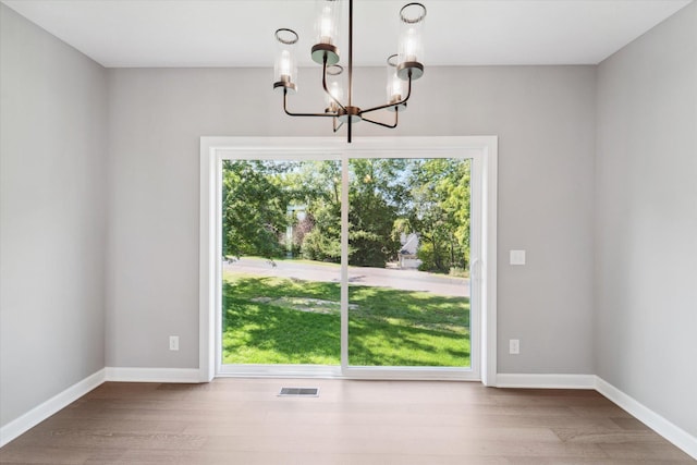 unfurnished dining area with wood-type flooring and a notable chandelier