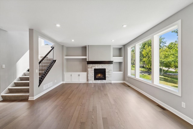 unfurnished living room with built in shelves, wood-type flooring, and a fireplace