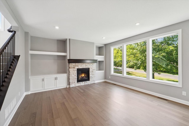 unfurnished living room with hardwood / wood-style floors, a stone fireplace, and built in shelves