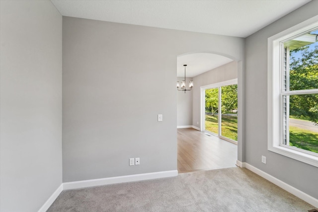 carpeted spare room with an inviting chandelier and plenty of natural light