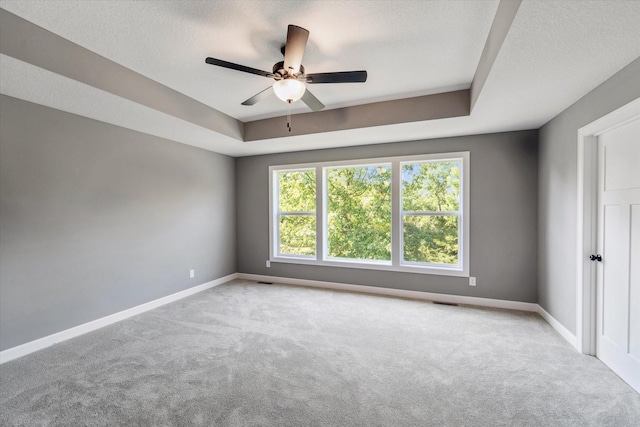 carpeted spare room featuring a textured ceiling, ceiling fan, and a tray ceiling