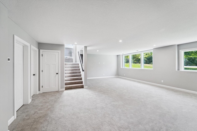 basement featuring a healthy amount of sunlight, light colored carpet, and a textured ceiling