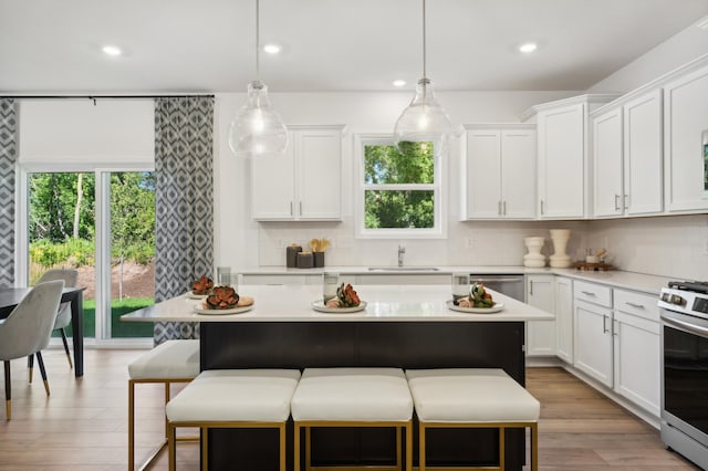 kitchen featuring white cabinets, a kitchen island, decorative light fixtures, stainless steel appliances, and sink