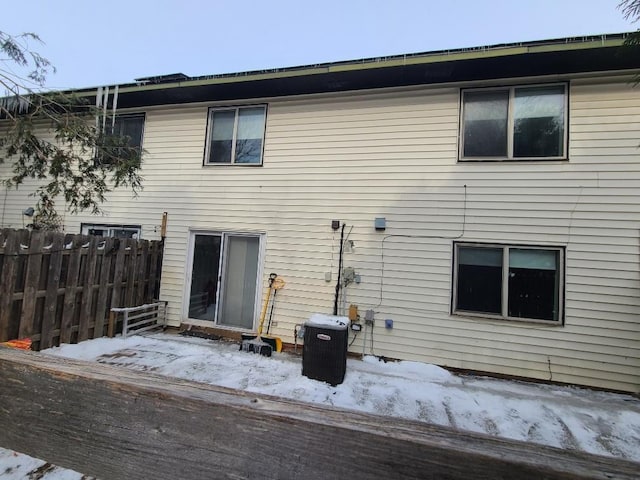 snow covered house featuring fence and central AC unit