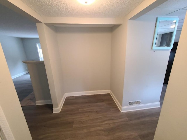 hall with a textured ceiling, dark wood-style flooring, visible vents, and baseboards