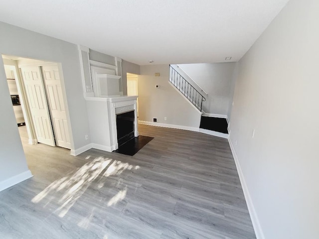 unfurnished living room featuring wood finished floors, stairway, a fireplace with flush hearth, and baseboards