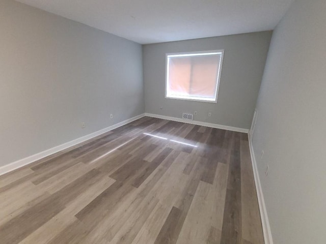 empty room with wood finished floors, visible vents, and baseboards