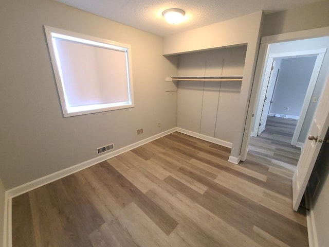 unfurnished bedroom featuring baseboards, visible vents, wood finished floors, a textured ceiling, and a closet