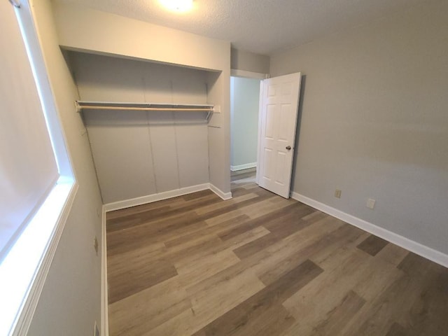 unfurnished bedroom with a closet, a textured ceiling, baseboards, and wood finished floors