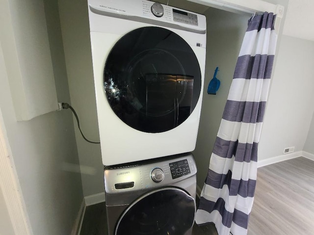 laundry room featuring stacked washer and dryer, baseboards, laundry area, and light wood finished floors