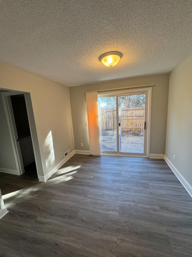 empty room featuring visible vents, a textured ceiling, and dark wood-type flooring