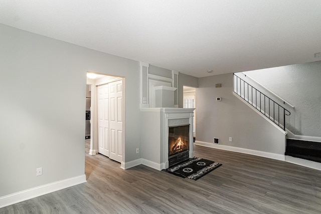 unfurnished living room featuring stairway, baseboards, a warm lit fireplace, and wood finished floors