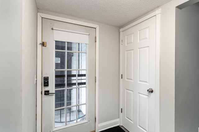 doorway with a textured ceiling and baseboards