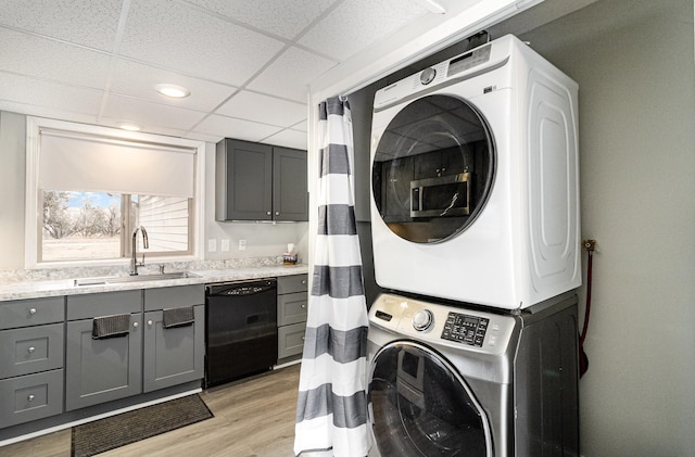 laundry room with a sink, laundry area, stacked washer and dryer, and light wood-style flooring